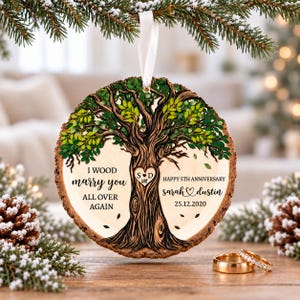 May include: A round wooden ornament with bark edges featuring a printed tree with green leaves. The text reads I WOOD marry you ALL OVER AGAIN, HAPPY 5TH ANNIVERSARY, sarah and dustin, and 25.12.2020. A heart on the tree trunk contains the initials S and D.