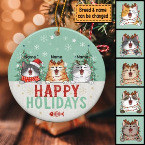 May include: A round, green and white Christmas ornament with three cats wearing Santa hats and reindeer antlers. The cats are surrounded by Christmas trees and snowflakes. The ornament says "Happy Holidays" in red and white letters.