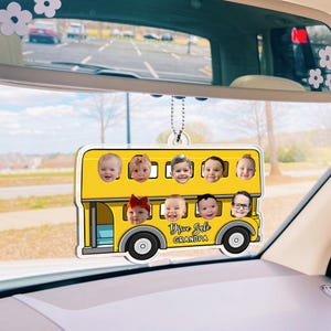 May include: A yellow double-decker bus-shaped car air freshener with nine baby faces in the windows. The text "Drive Safe Grandpa" is printed on the bus. The air freshener hangs from a chain.
