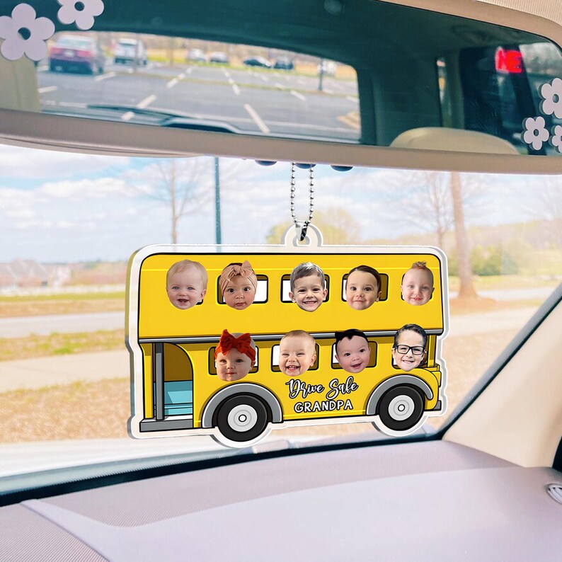May include: A yellow double-decker bus-shaped car air freshener with nine baby faces in the windows. The text "Drive Safe Grandpa" is printed on the bus. The air freshener hangs from a chain.