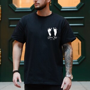 May include: Black t-shirt with a white design of two baby footprints and the text "Olivia June" and "April 11, 2024".
