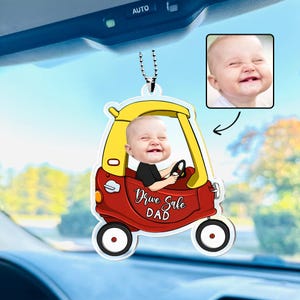 May include: A personalized car ornament featuring a smiling baby in a red and yellow cartoon car. The ornament has the text "Drive Safe DAD" and includes a small photo of the baby. The ornament hangs from a silver chain.