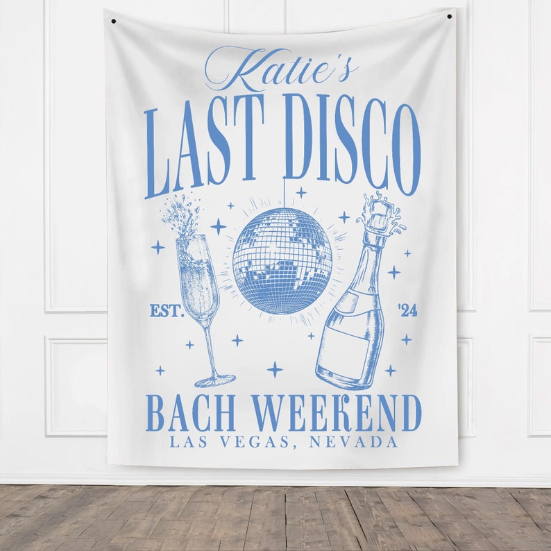 May include: A white banner with blue text that reads "Katie's Last Disco Bach Weekend Las Vegas, Nevada". The banner also features a blue disco ball, a champagne bottle, and a champagne flute.