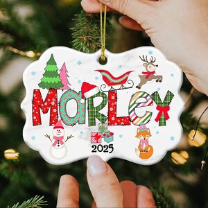May include: A personalized Christmas ornament with the name "MORLEY" in festive lettering. The design includes a snowman, a reindeer, a sleigh, and a fox, with the year "2025" displayed. The ornament is white with a gold string.