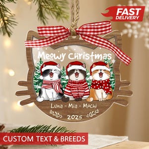 May include: A wooden Christmas ornament shaped like a cat's head, featuring three cartoon cats wearing Santa hats and sweaters. The ornament has the text "Meowy Christmas", the names "Luna - Mia - Mochi", and the year "2025". A red and white checkered ribbon is at the top.
