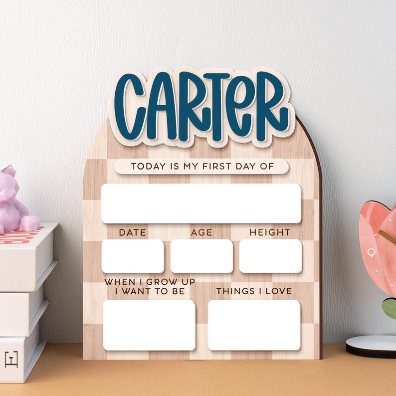 Op de afbeelding: Houten mijlpaalbord met de naam "CARTER" in blauw schrift. Het bord heeft vakken voor "DATUM", "LEEFTIJD" en "LENGTE", samen met vragen voor "ALS IK GROOT BEN WIL IK WORDEN" en "Dingen die ik leuk vind". De achtergrond heeft een lichtbruin gestreept patroon.