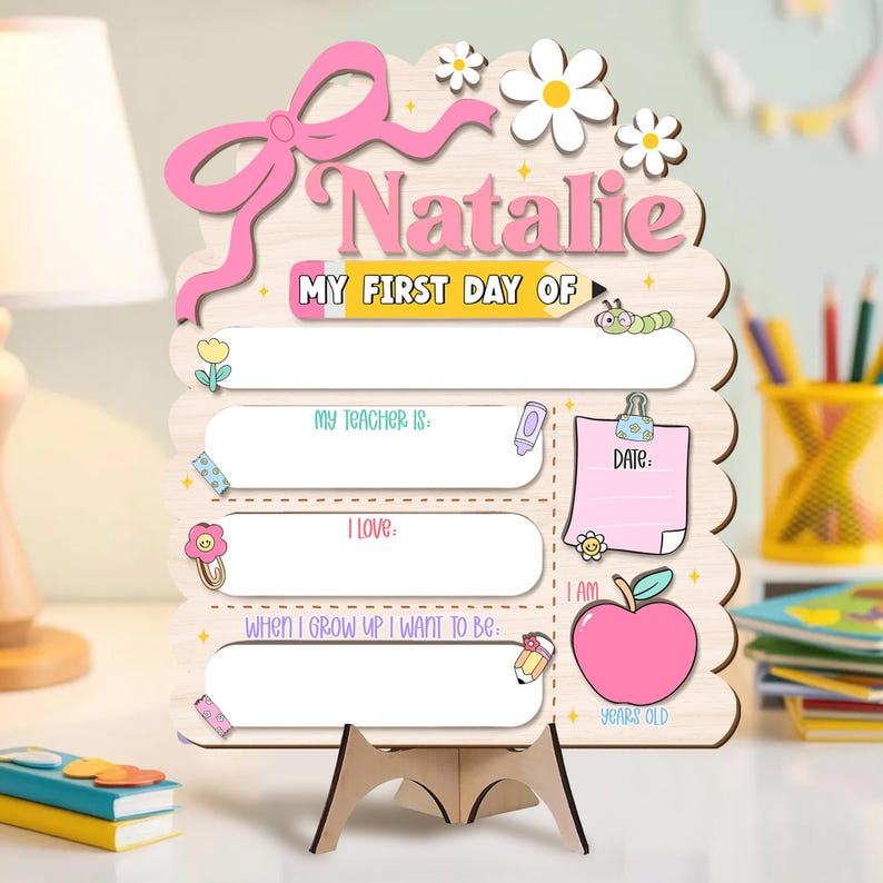 May include: Wooden sign with a pink bow, the name "Natalie", and the text "MY FIRST DAY OF". Includes spaces to write "MY TEACHER IS", "I LOVE", and "WHEN I GROW UP I WANT TO BE". Features a pink apple and a space for the date.