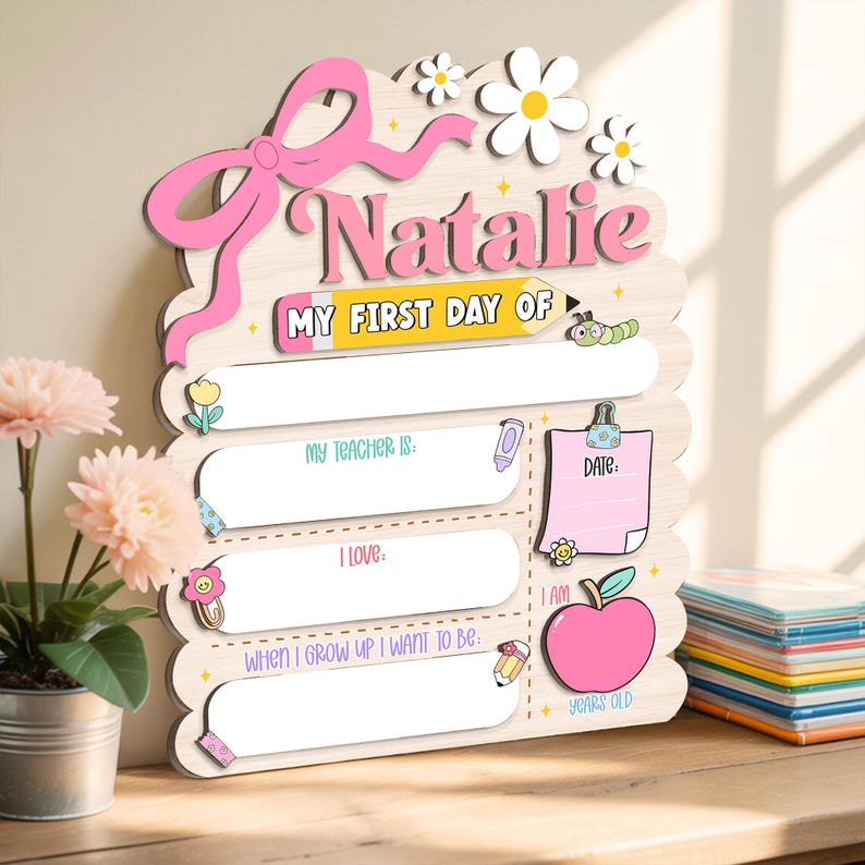 May include: Wooden sign with the name "Natalie" in pink, featuring a pink bow, daisies, and the text "MY FIRST DAY OF." Includes fill-in-the-blank sections for teacher, loves, and future aspirations, plus an apple graphic and "YEARS OLD."