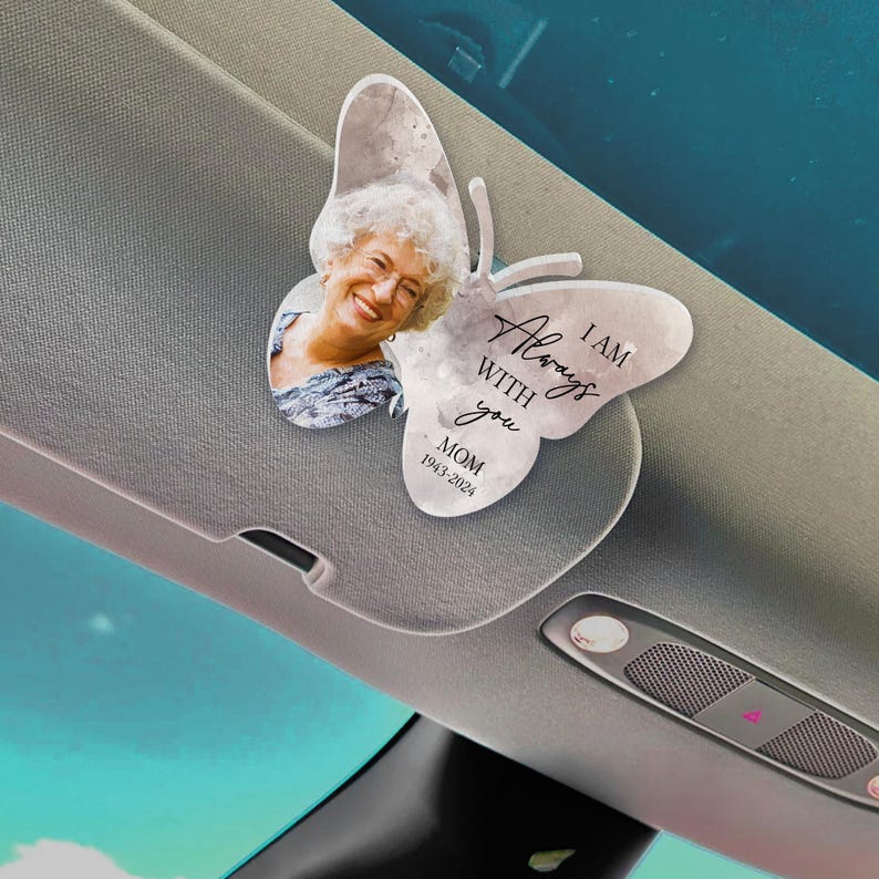 May include: A white butterfly-shaped car charm with a photo of a woman and the text "I AM ALWAYS WITH YOU MOM 1943-2024".