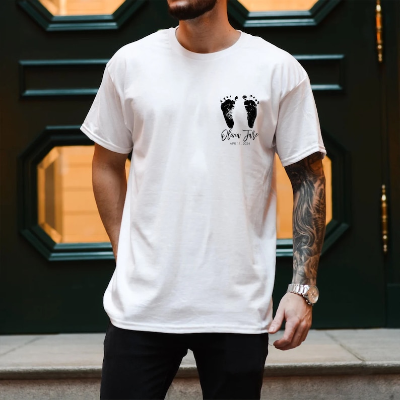 May include: White t-shirt with a black design of two baby footprints and the text "Olivia Jane" and "APR 11, 2024".