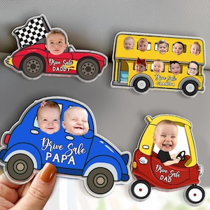 May include: A collection of car-shaped magnets with smiling baby faces. The magnets are red, yellow, and blue, with the text "Drive Safe" and the names "Daddy," "Grandpa," "Papa," and "Dad."