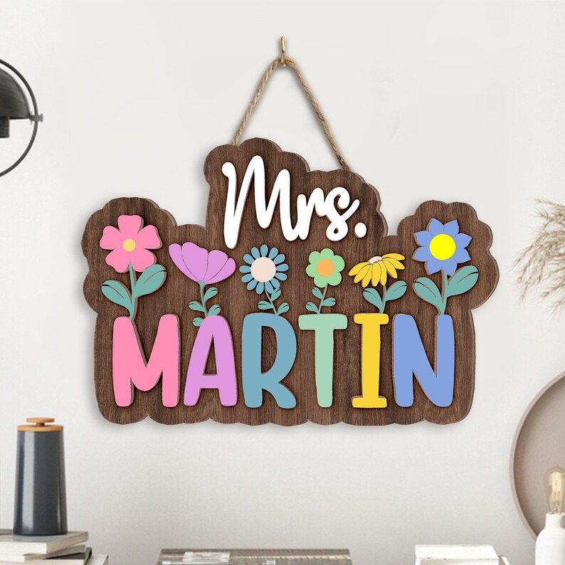 May include: A wooden sign with the text "Mrs. Martin" in colorful letters. The sign is decorated with flowers in various colors, including pink, blue, yellow, and green.