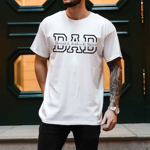 K&ouml;nnte beinhalten: Wei&szlig;es T-Shirt mit schwarzem Text, der "DAD" lautet, mit den Namen "Thomas & Sophia & David" darunter.