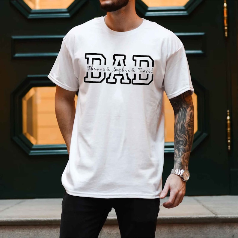 K&ouml;nnte beinhalten: Wei&szlig;es T-Shirt mit schwarzem Text, der "DAD" lautet, mit den Namen "Thomas & Sophia & David" darunter.