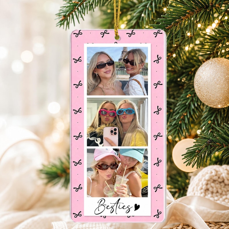 May include: A rectangular pink hanging ornament featuring a repeating black bow pattern and three stacked photographs of two individuals. The bottom of the ornament displays the text Besties in black script with a small black heart icon.