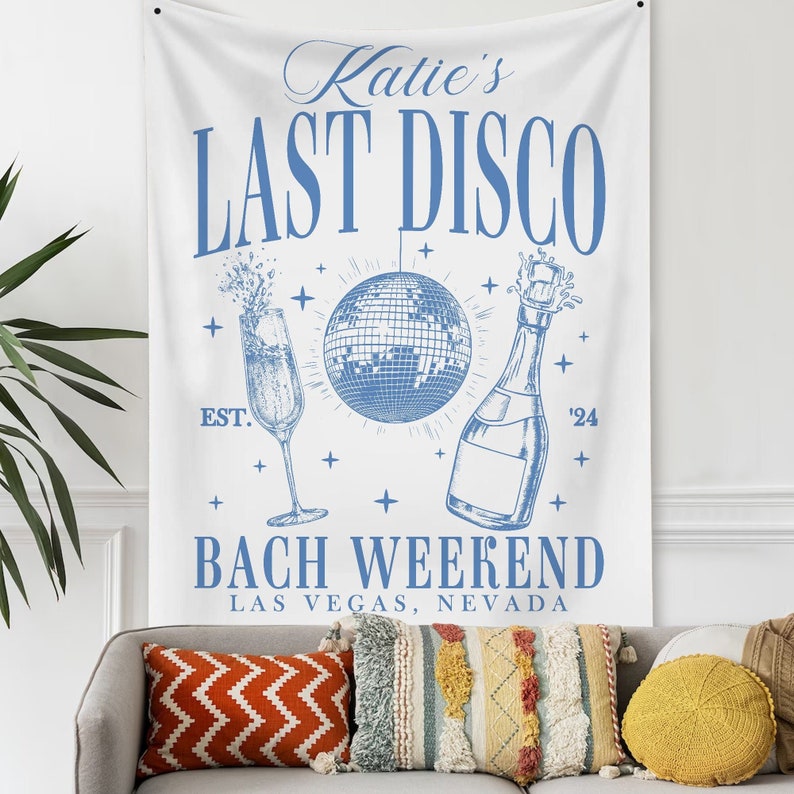 May include: White bachelorette party banner with blue text that reads "Katie's Last Disco Est. '24 Bach Weekend Las Vegas, Nevada". The banner also features a blue disco ball, a champagne flute, and a bottle of champagne.