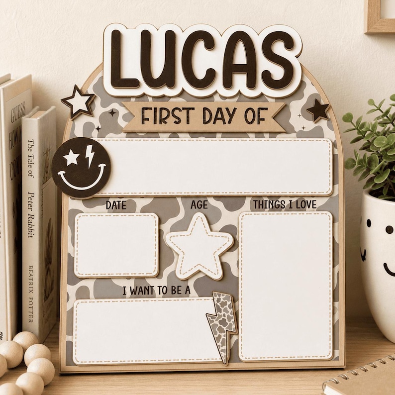 May include: An arched wooden sign with a gray and white cow print background. The text reads LUCAS, FIRST DAY OF, DATE, AGE, THINGS I LOVE, and I WANT TO BE A. It features a smiley face with a lightning bolt eye, two stars, and a lightning bolt.