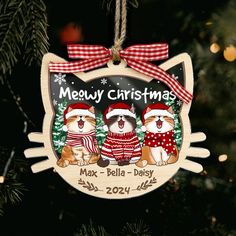 May include: Wooden Christmas ornament shaped like a cat's head, featuring three cartoon cats wearing Santa hats and scarves. The ornament says "Meowy Christmas" and includes the names Max, Bella, and Daisy, with the year 2024.