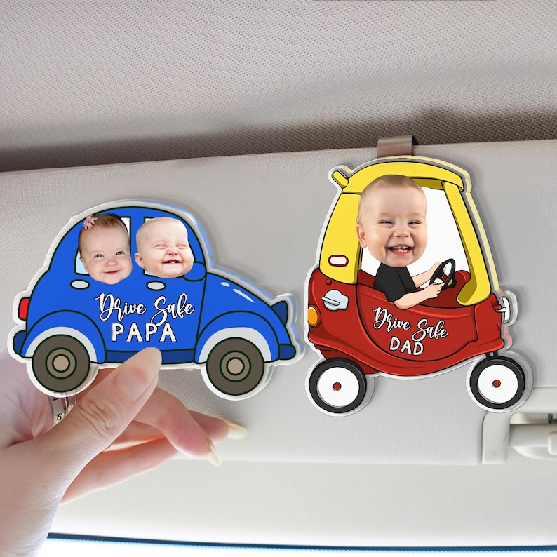 May include: Two car-shaped visor clips, one blue and one red, each with a baby's photo. The blue car has two babies and the text "Drive Safe PAPA." The red car has one baby and the text "Drive Safe DAD."