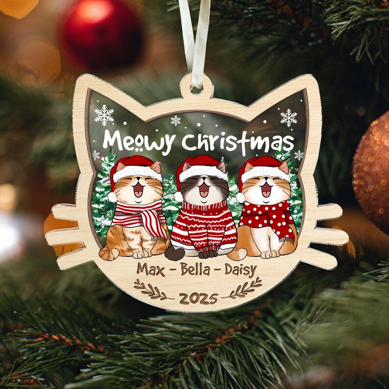 May include: Wooden cat-shaped Christmas ornament with three cartoon cats wearing Santa hats and scarves. The ornament says "Meowy Christmas" and has the names "Max - Bella - Daisy" and the year "2025" on it. The ornament hangs from a white ribbon.