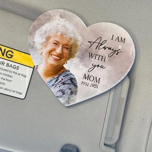 May include: A heart-shaped car air freshener with a watercolor background. The image of a woman is on the left side of the heart. The text "I AM Always WITH you MOM 1952-2024" is on the right side of the heart.