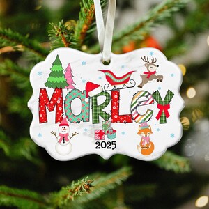 May include: A decorative Christmas ornament with the name "MORLEY" in festive lettering. The ornament features a snowman, fox, reindeer, and a sleigh, along with the year "2025". The background is white with snowflakes.