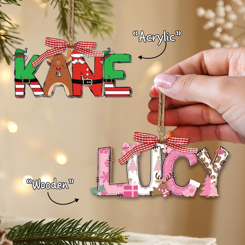 May include: Two Christmas ornaments spelling "KANE" and "LUCY". The "KANE" ornament is green, brown, and red with a plaid bow. The "LUCY" ornament is pink and white with a plaid bow. Both are hanging from twine.