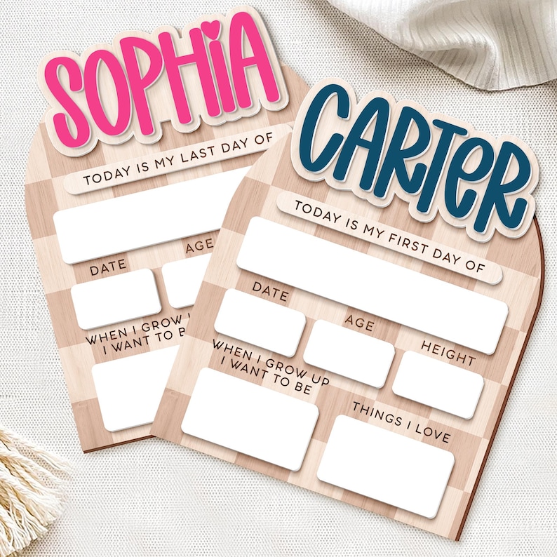 Op de afbeelding: Twee houten schoolborden met de namen "Sophia" in roze en "Carter" in blauw. Ze hebben vakken voor datum, leeftijd en ambities, met de tekst "Today is my last day of" en "Today is my first day of."