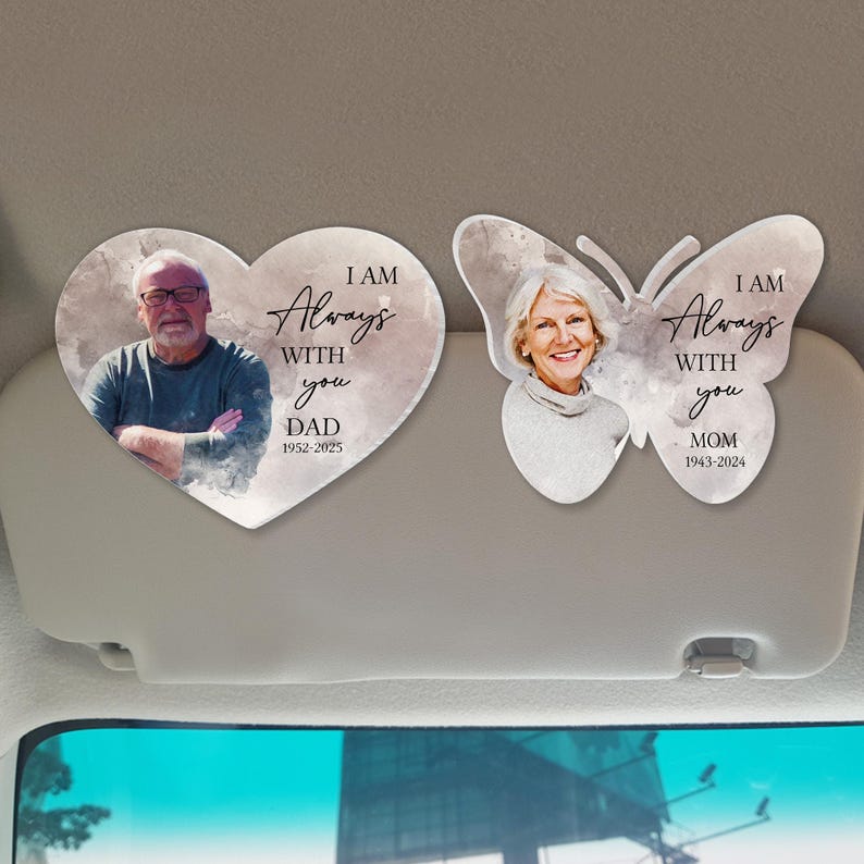 May include: Two car visor clips with a watercolor background. One clip is a heart shape with a photo of a man and the text "I am Always With You Dad 1952-2025". The other clip is a butterfly shape with a photo of a woman and the text "I am Always With You Mom 1943-2024".