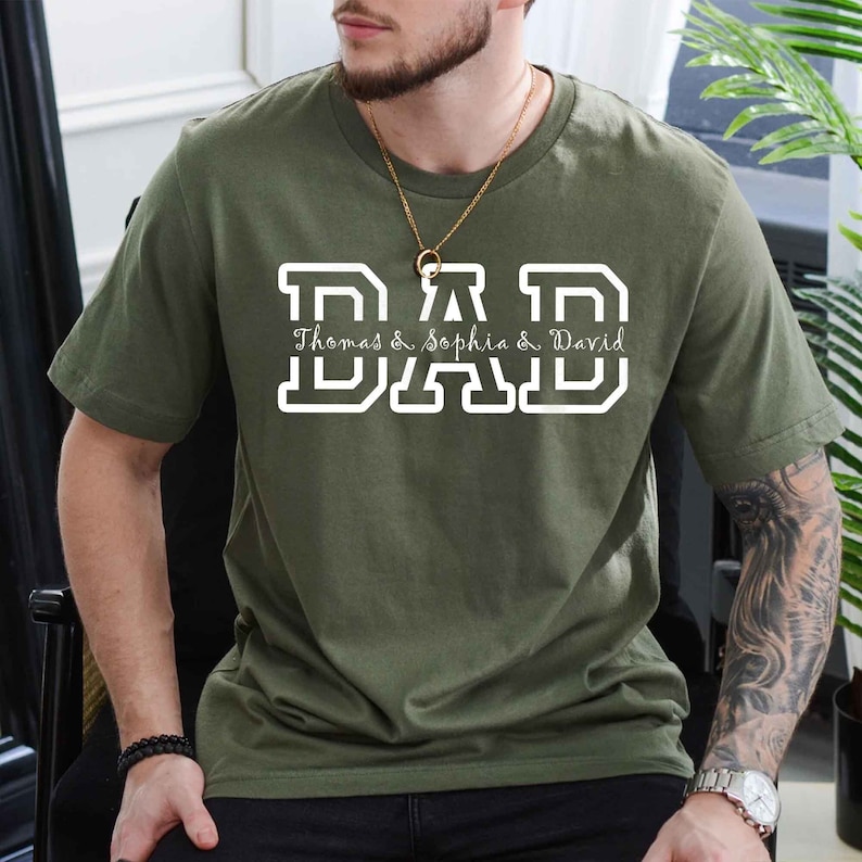 K&ouml;nnte beinhalten: Ein gr&uuml;nes T-Shirt mit einer wei&szlig;en "DAD"-Grafik. Der Text "Thomas & Sophia & David" steht unter der Grafik.