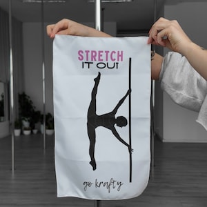 Op de afbeelding: Witte handdoek met een zwart silhouet van een persoon die aan een paal strekt. De tekst "Stretch it out" is roze en de tekst "go krafty" is zwart.