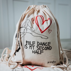 Può includere: Una borsa a cordoncino bianca con un designo nero e rosso. La borsa presenta una silhouette di una donna che balla al palo con il testo "Pole Dance is my Second Half" e un cuore rosso. La borsa ha il testo "go krafty" stampato sul fondo.