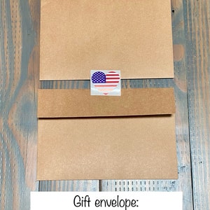 Może przedstawiać: Brązowa koperta prezentowa z naklejką w kształcie serca z amerykańską flagą. Pod kopertą znajduje się tekst "Gift envelope: Front, Back and Heart Seal".