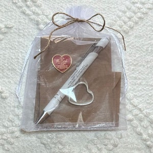 May include: A white organza bag with a brown twine bow contains a small red heart pin with the words "You are my sunshine" and a white pen. The bag also contains a brown card with the text "VOLUNTEER A true HEART for what we do. Many THANKS - We APPRECIATE You."