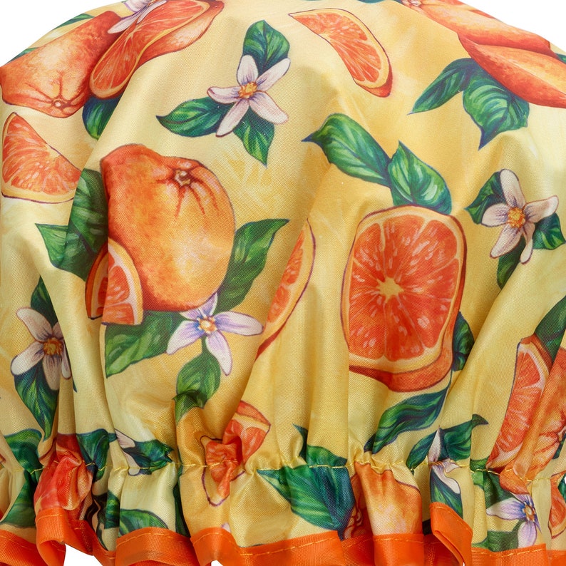 May include: A yellow shower cap with a vibrant orange and white floral pattern. The design features oranges, orange slices, white flowers, and green leaves. The cap has an orange trim.