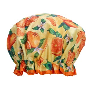 May include: A yellow shower cap with a repeating pattern of oranges, orange slices, green leaves, and white flowers. The cap has a ruffled orange trim around the bottom edge. The shower cap is made of a lightweight, possibly waterproof material.
