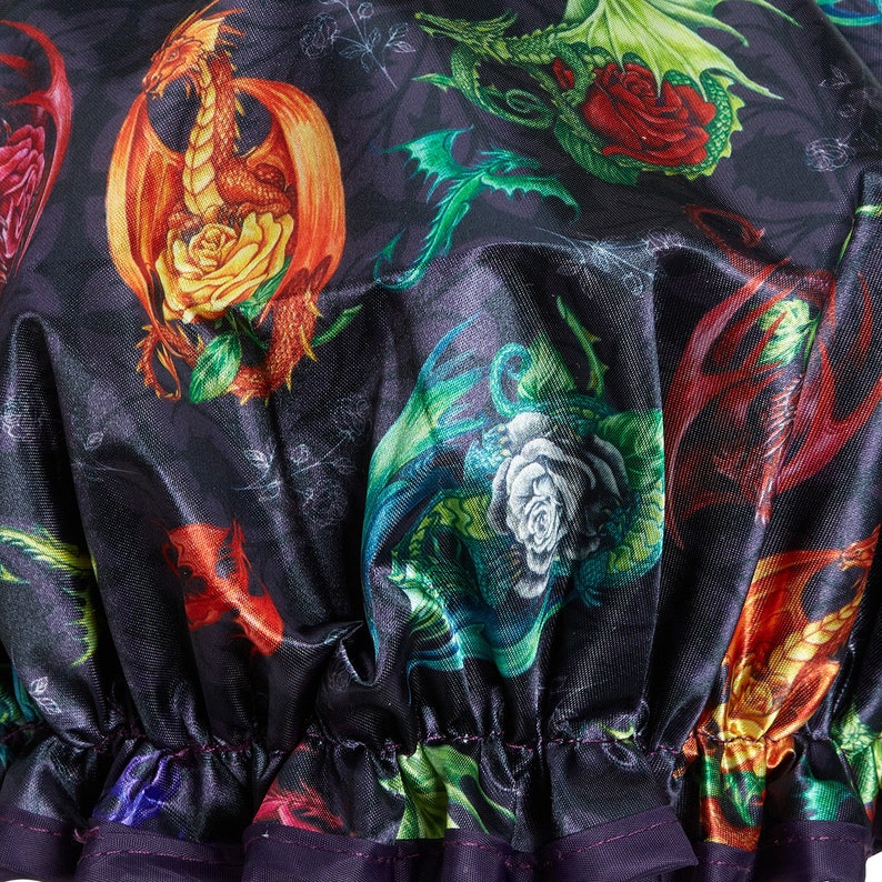 May include: A black satin shower cap with a colorful print of dragons and roses. The cap has a purple elastic band.
