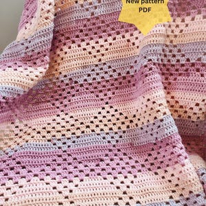 May include: A handmade crochet blanket in shades of pink, purple, and beige. The blanket features a geometric openwork design and is draped, showcasing its texture. Text on the image reads "New pattern PDF" and "AllaBellaLondon | Etsy".