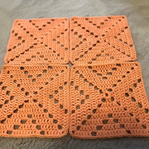 May include: Four crocheted squares in a peach colour, each with a diamond pattern in the centre. The squares are joined together to form a larger piece.