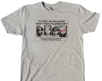 May include: A gray t-shirt with a black and white graphic print of a poster that reads "IT'S 1987. DO YOU KNOW WHAT YOUR CHILDREN ARE?" The poster features four children's faces with the word "MUTIE" written in red over the last child's face. The poster also reads "Paid for by citizens in support of The Mutant Registration Act."