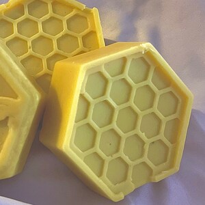May include: Three yellow honeycomb-shaped soap bars. The bars are made of a creamy, yellow soap and have a honeycomb pattern on the surface.