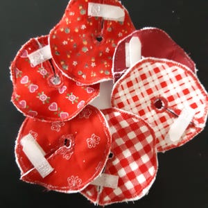 Puede incluir: Un conjunto de seis círculos de tela roja y blanca con un agujero en el centro. Cada círculo tiene un patrón diferente, incluyendo cuadros, lunares y corazones. Los círculos están unidos entre sí con cinta blanca.