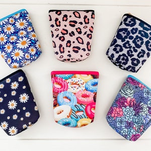 May include: Six cylindrical beverage insulators featuring various patterns including white daisies on blue, pink leopard print, grey leopard print, white daisies on black, colorful glazed donuts with sprinkles, and a multi-colored succulent plant design.