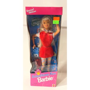 May include: A Barbie doll wearing a red dress with a white shirt and plaid tights. She is holding a blue bag and a red book. The box is pink and says "Schooltime Fun Barbie" and "Special Edition".