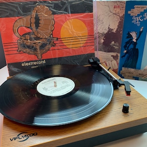 May include: A wooden record player with a black vinyl record on the turntable. The record player has a black needle arm and a black control knob. The record player has a black and brown color scheme. The record player has the text "VIFLYKOO" on the front.