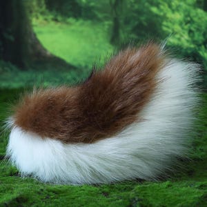 May include: A fluffy, faux fur tail in brown and white. The tail is a mix of brown and white fur, with the brown fur at the top and the white fur at the bottom. The tail is likely for a costume or cosplay.