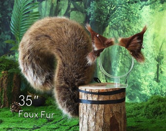 Puede incluir: Una cola de piel sintética marrón de 89 cm de largo. La cola está enroscada y se muestra en un tocón de árbol. Un par de orejas a juego de piel sintética con cascabeles plateados se muestran en una diadema de plástico transparente.