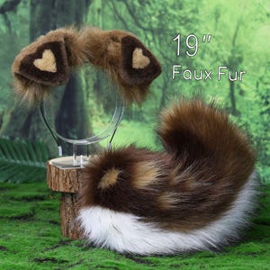 May include: A set consisting of a headband with brown faux fur ears featuring tan heart-shaped centres and a 48 cm long faux fur tail. The tail has a mix of brown, tan, and white fur, with a prominent white tip. The text 19" Faux Fur is visible.