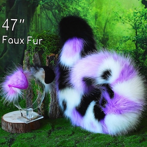 Puede incluir: Un conjunto de cola y orejas de piel sintética en negro, blanco y lavanda. La cola mide aproximadamente 120 cm de largo. La diadema de orejas presenta un diseño de oreja púrpura. El texto "47" y "Faux Fur" es visible.