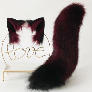 May include: A set of burgundy and black faux fur cat ears and tail. The ears are attached to a headband and the tail is long and fluffy.